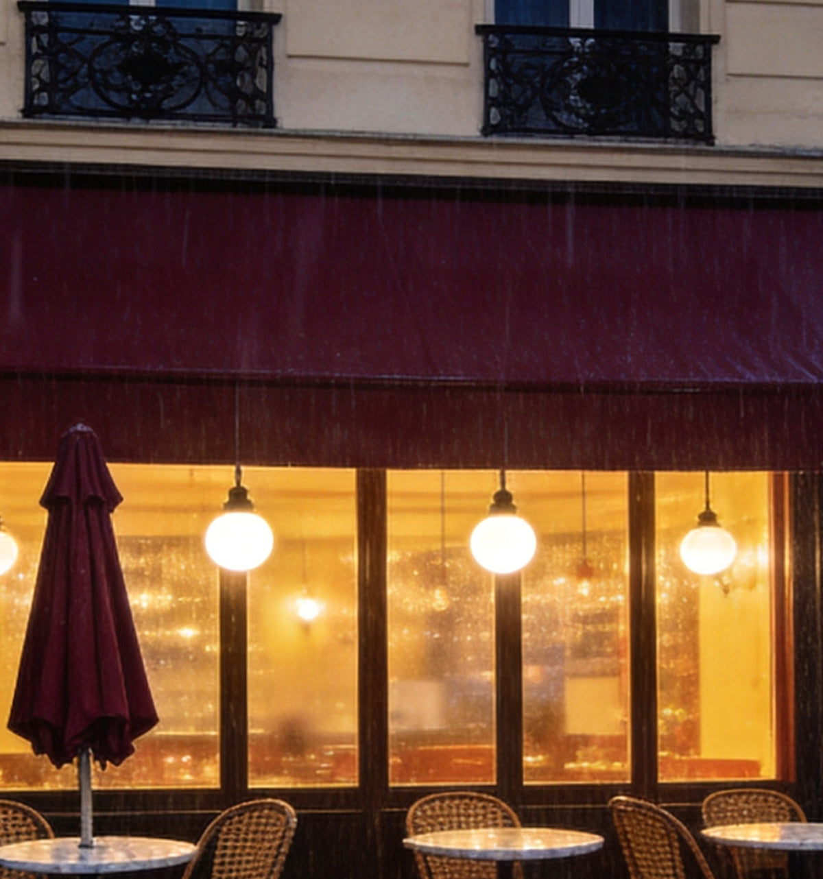 Détail : auvent bordeaux, suspensions en globe derrière les vitres et chaises en rotin sous la pluie
