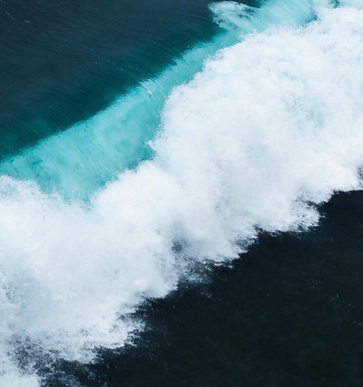Détail : la ligne d'écume blanche bordée d'une bande turquoise translucide, sur l'eau bleu sombre