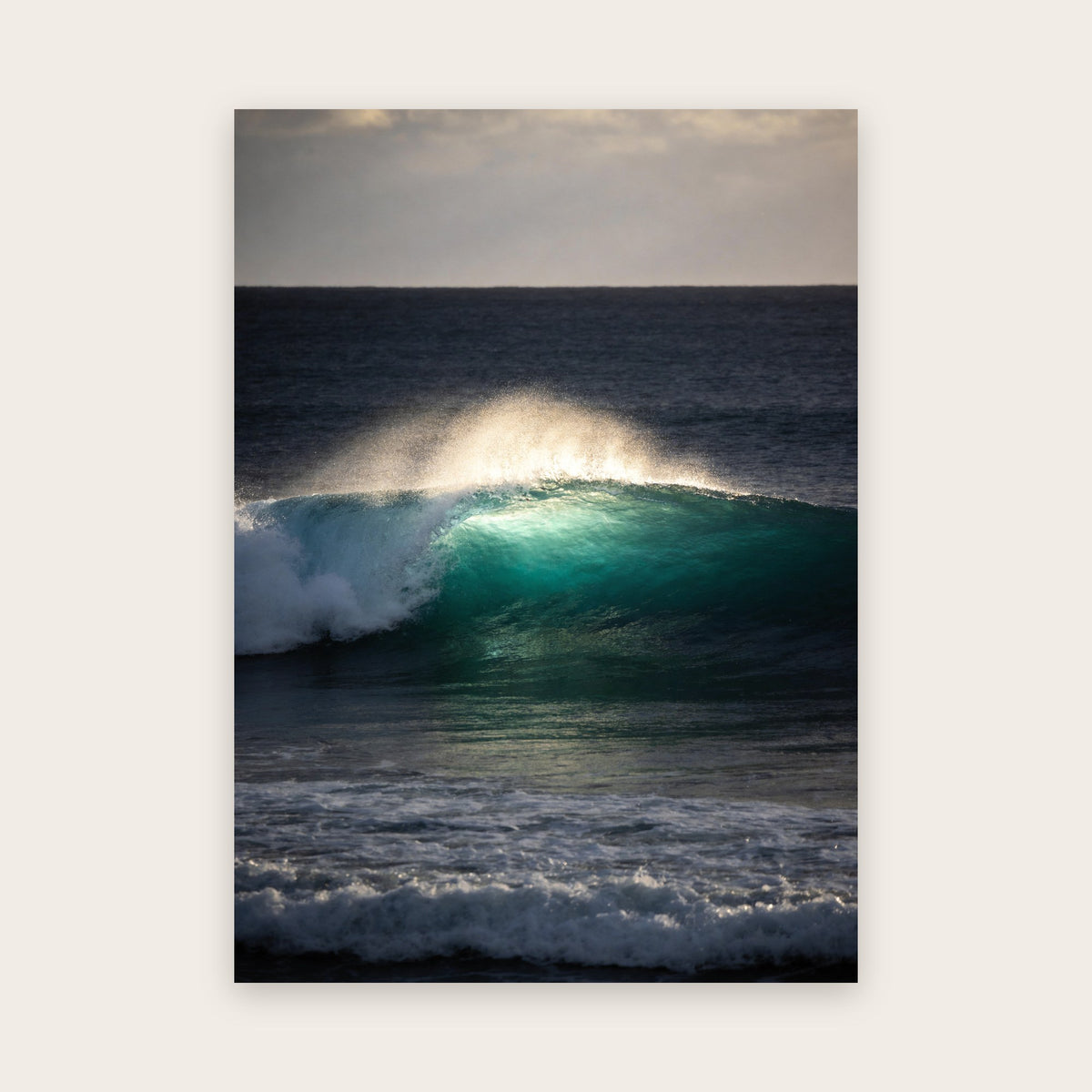 Affiche vague : une vague émeraude illuminée par une éclaircie, voile d'embruns doré, sur une mer gris-bleu sous un ciel nuageux