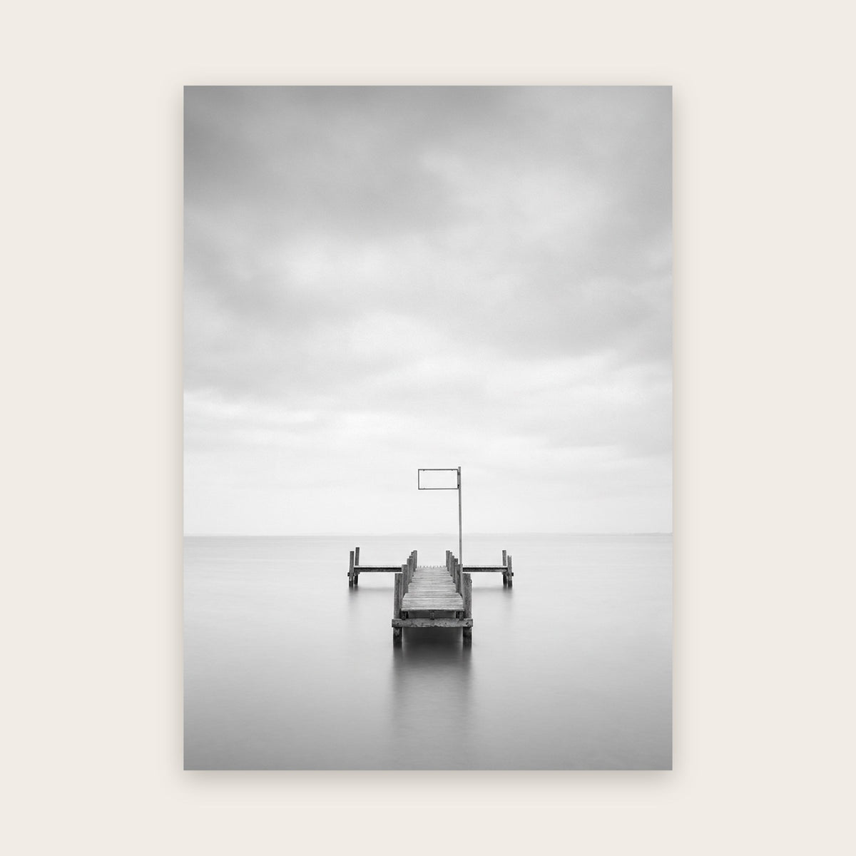 Tableau noir et blanc : jetée en bois s'avançant sur une mer lisse sous un ciel couvert, poteau métallique au rectangle vide