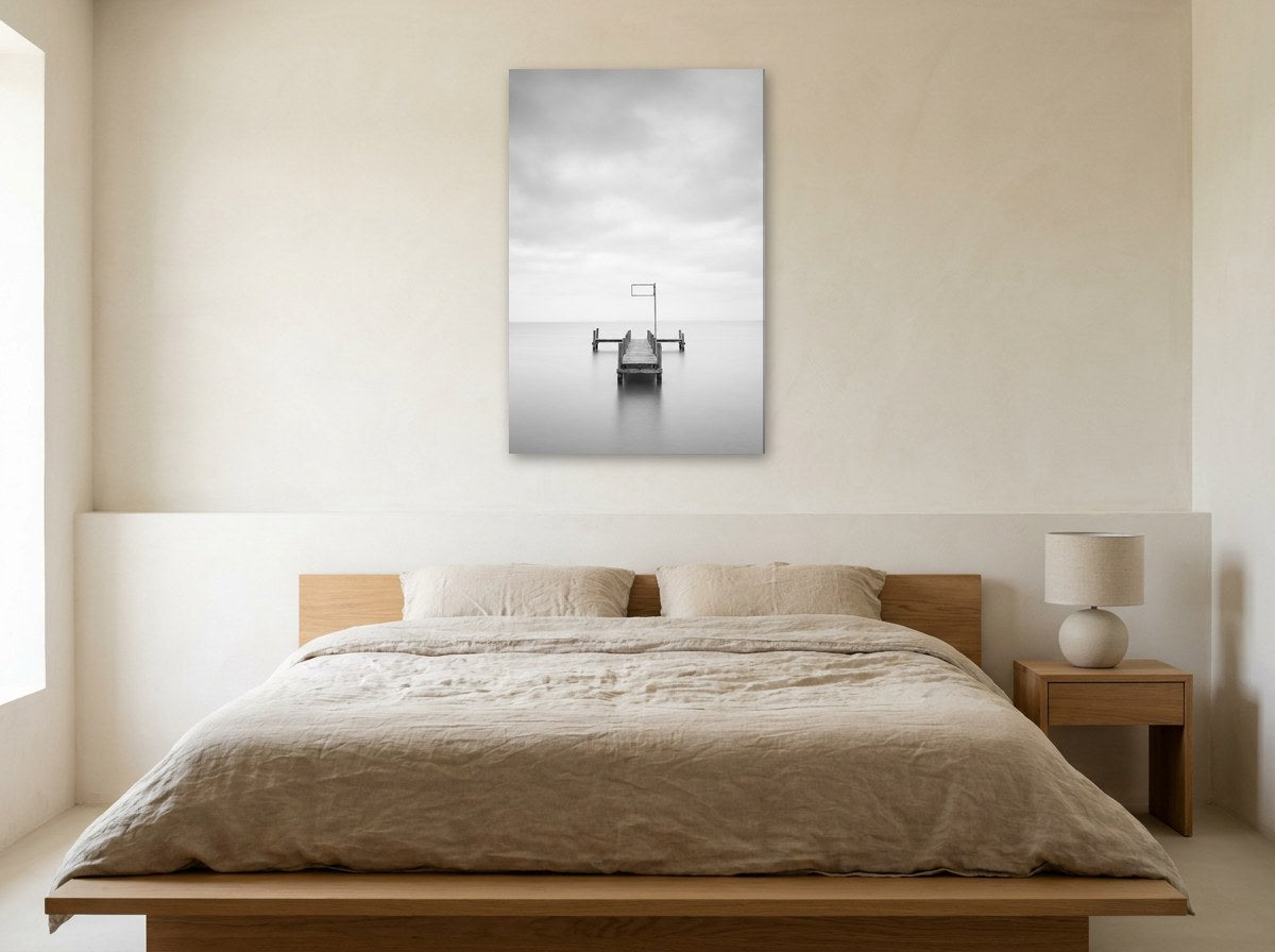 Tableau noir et blanc d'une jetée sur mer calme accroché au-dessus d'un lit, dans une chambre aux tons lin et bois clair