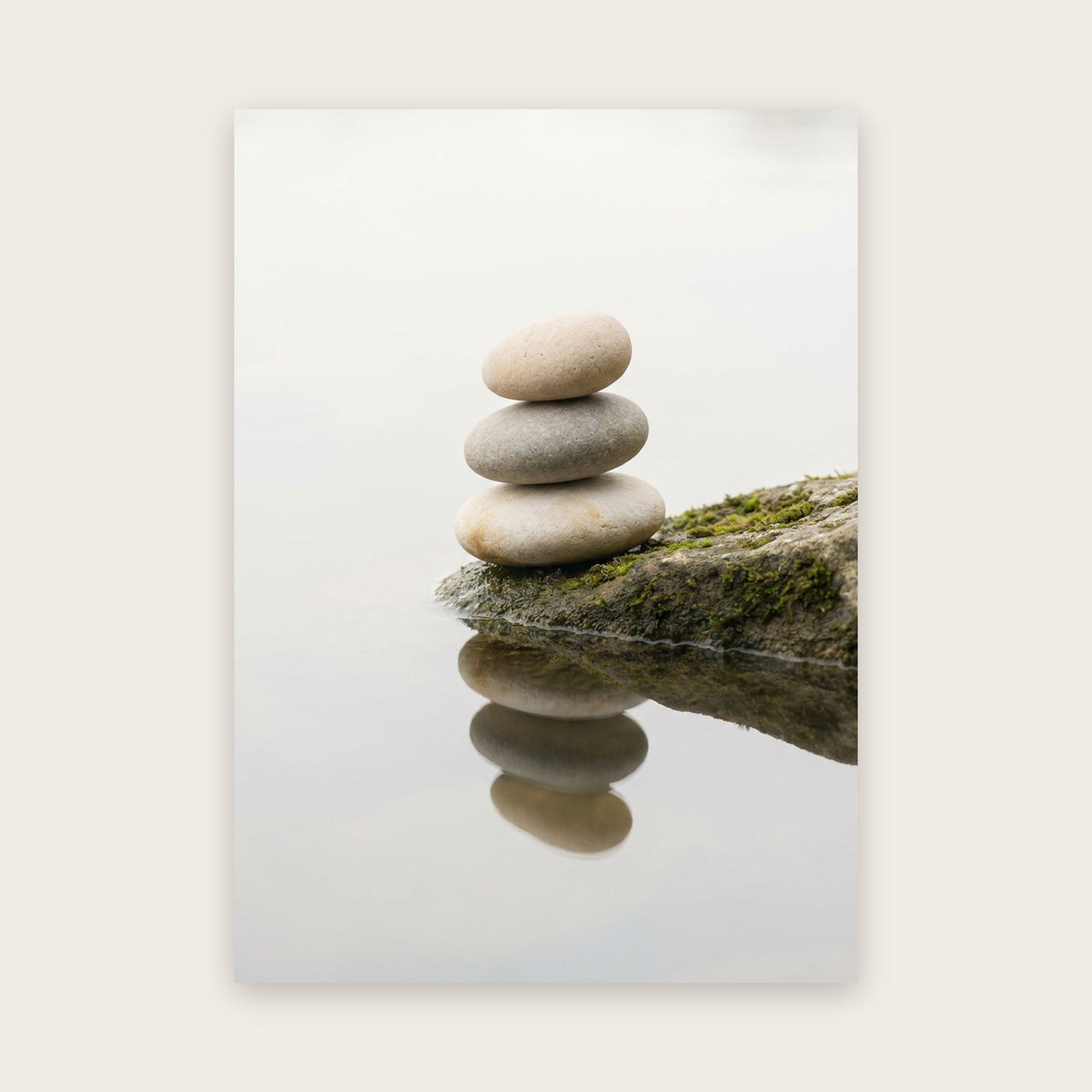 Tableau zen : trois galets beiges et gris empilés sur un rocher moussu, reflétés dans une eau lisse sous une brume claire