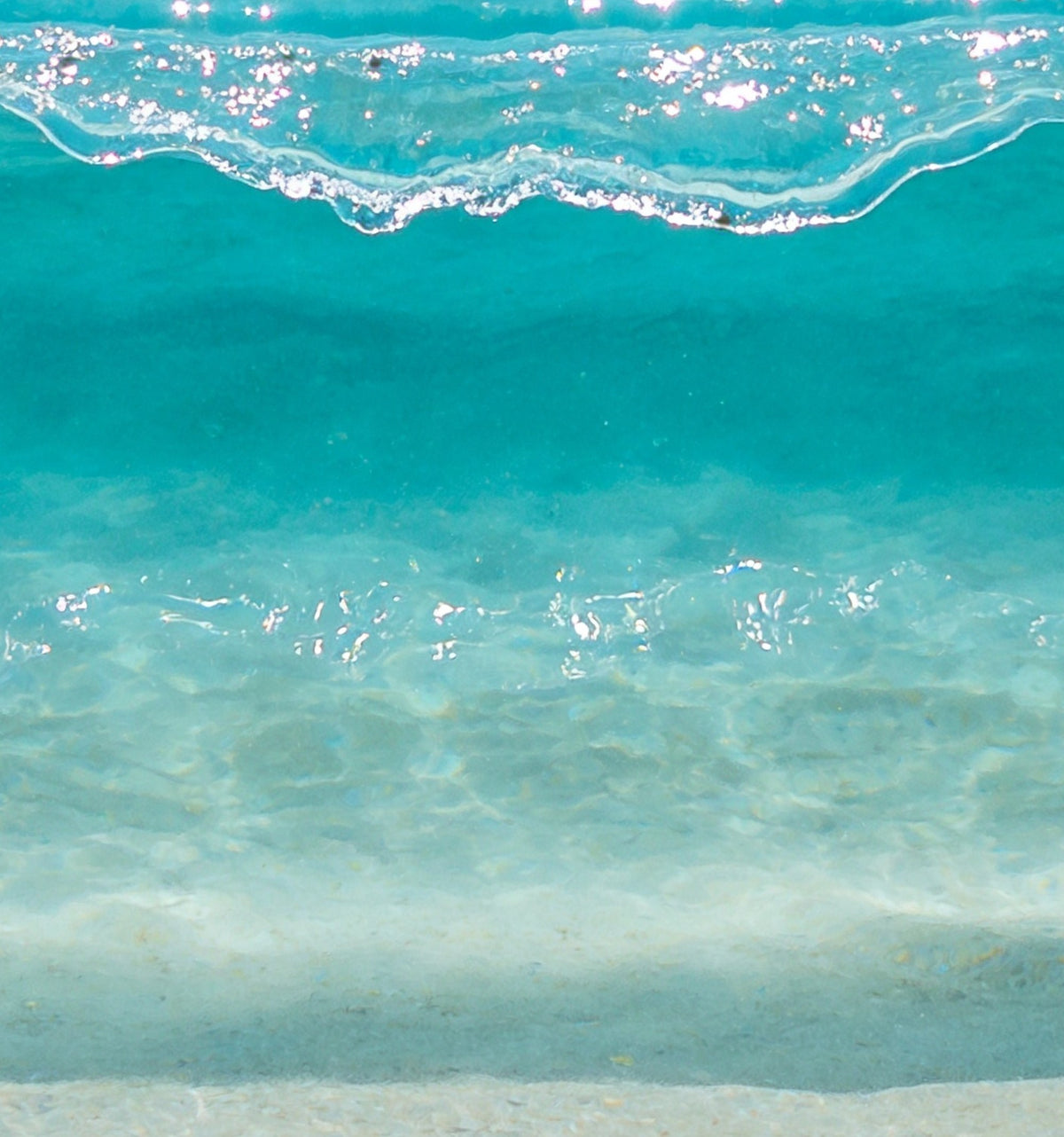 Détail : la lèvre scintillante de la vague et l'eau turquoise transparente, avec les reflets du soleil sur le fond